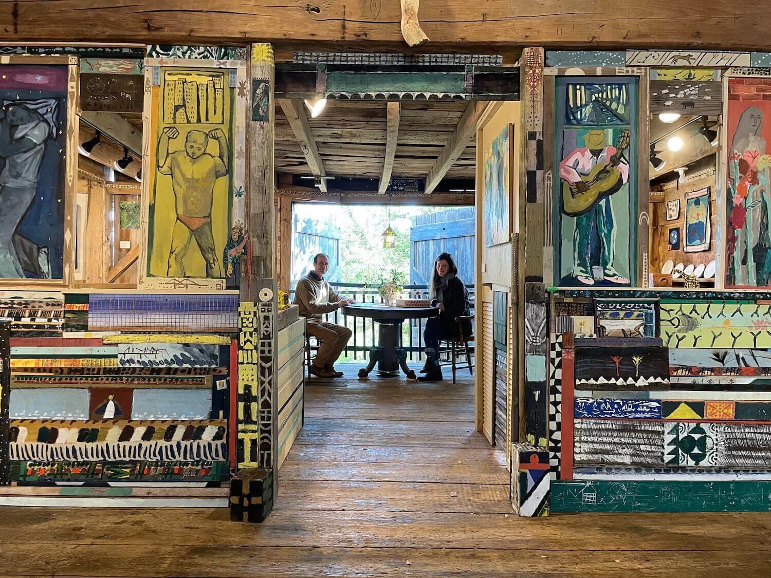 Clara Weishahn and Alex Cohen seated within the installation, Tribute to the Artist and Their Family, created by Tali Burry-Schnepp, Henry Murphy, and Ana Neifeld for the 2024 Art at Kings Oaks exhibition. Toad vessel by Karlene Jean Kantner displayed with flowers on the table.
